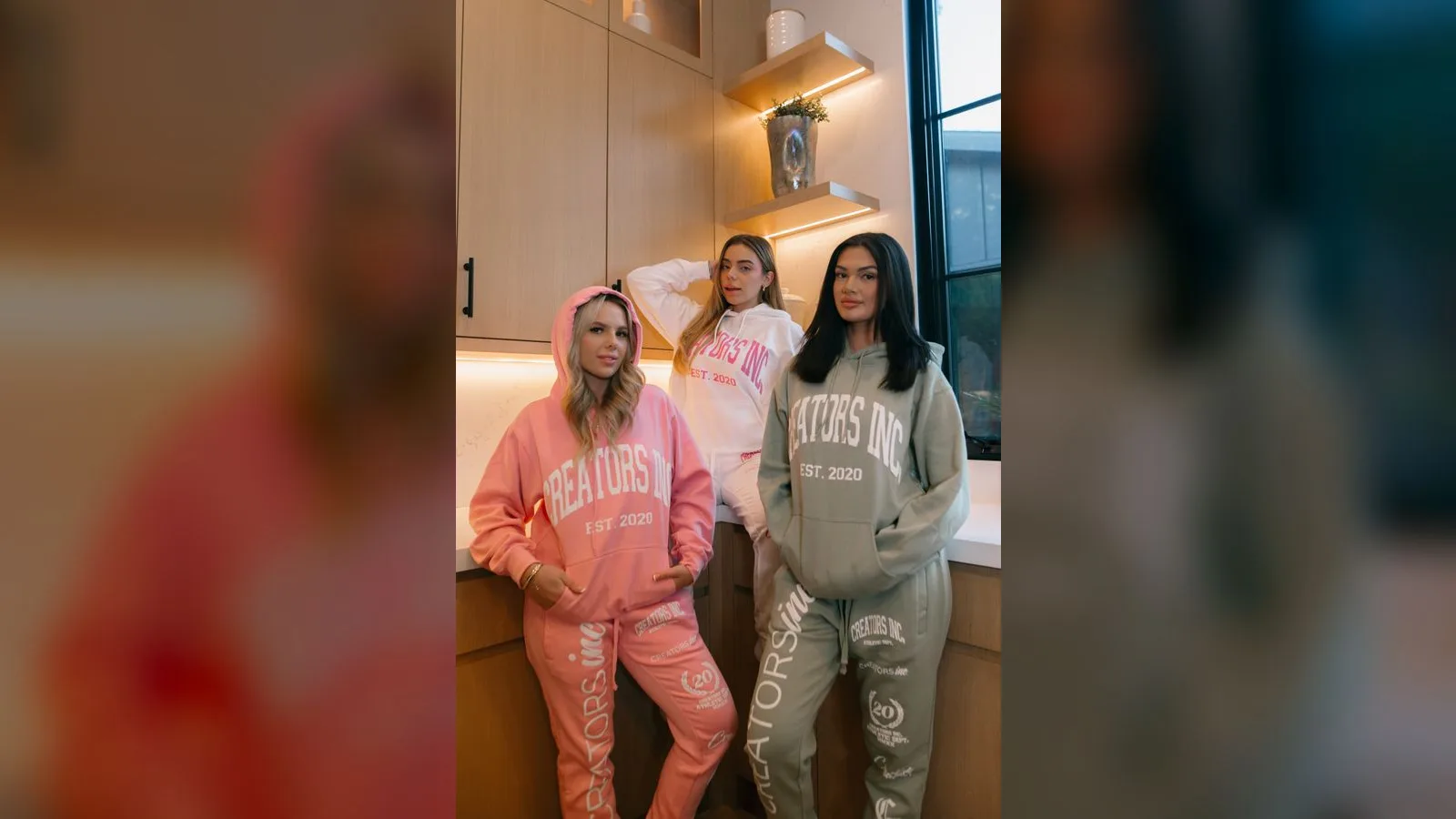 Three creators wearing pink and sage Creators Inc branded sweatsuits together in a bright kitchen