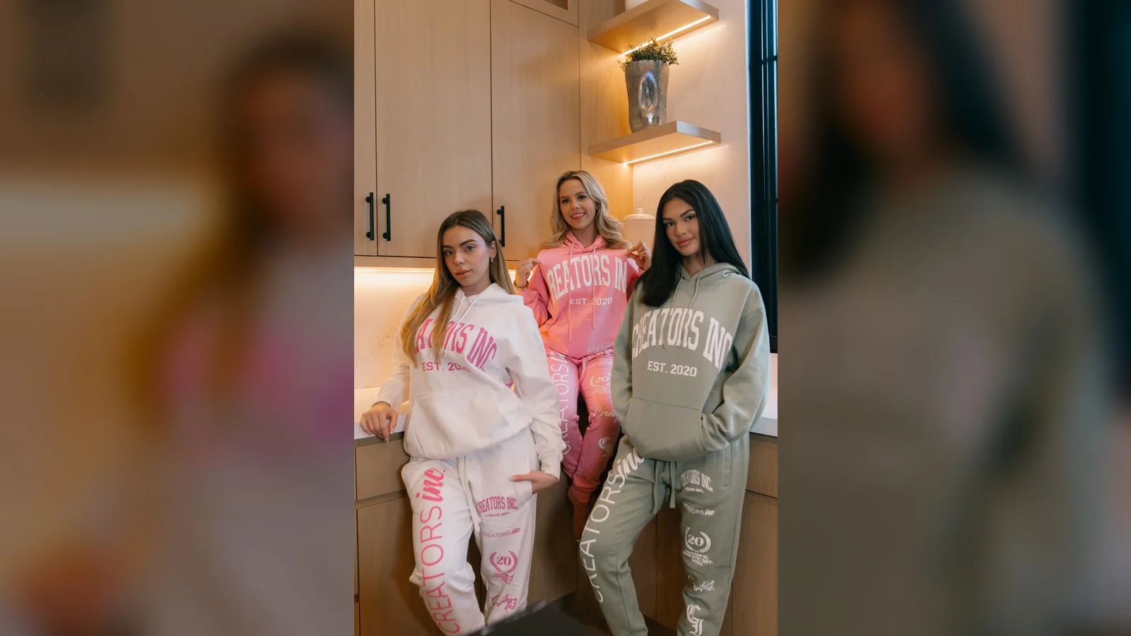 Three creators wearing Creators Inc branded sweatsuits in cream, pink and sage in a bright kitchen