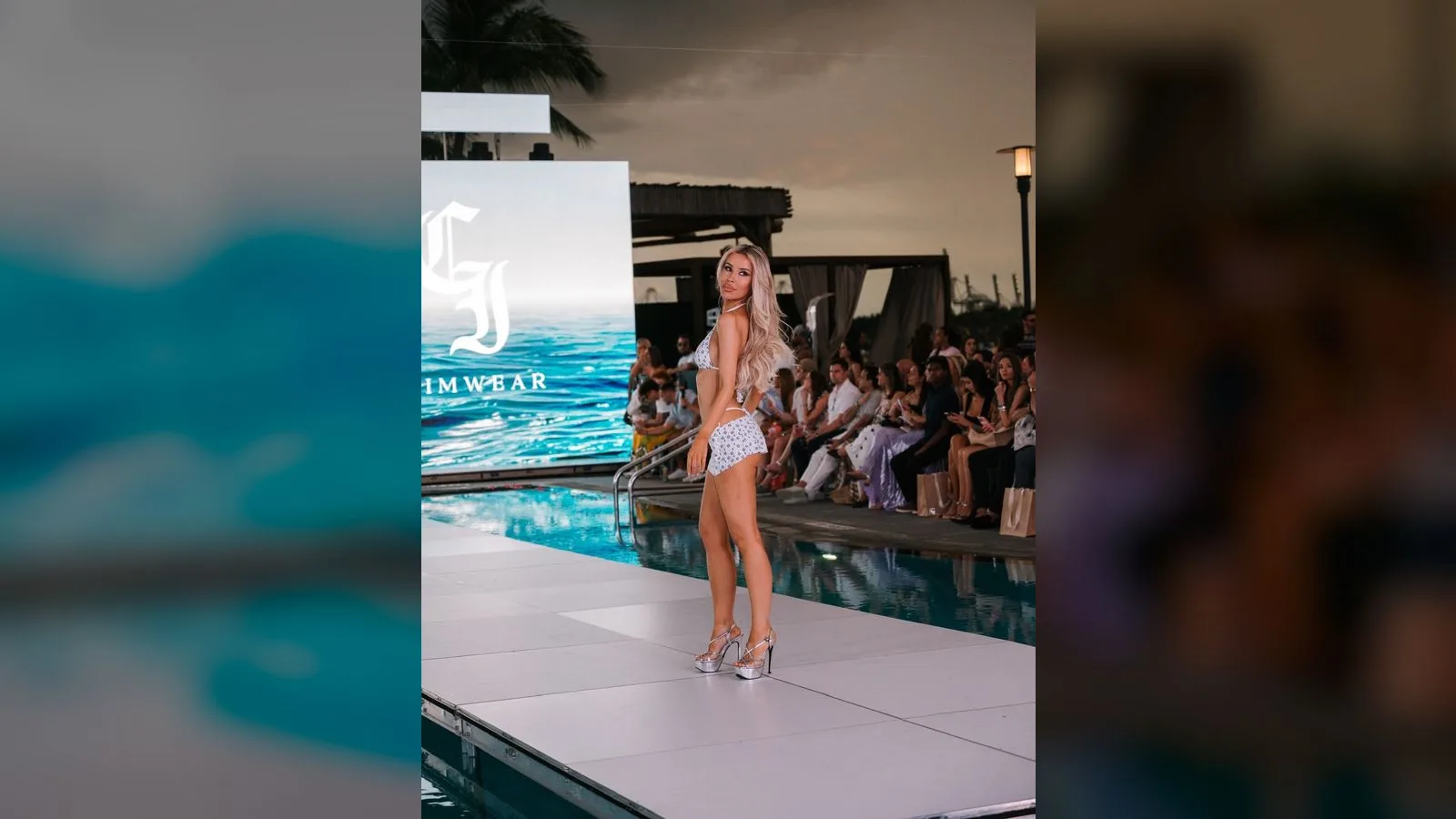 Creator walking a full-body CI Swimwear runway look past the branded screen at sunset